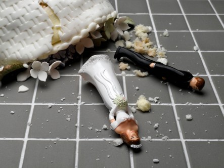 Bride and groom figurines lying at destroyed wedding cake on tiled floor